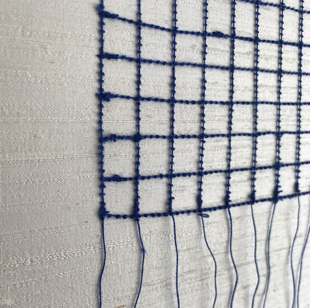 Close-up of a blue embroidered grid pattern on a white fabric background.