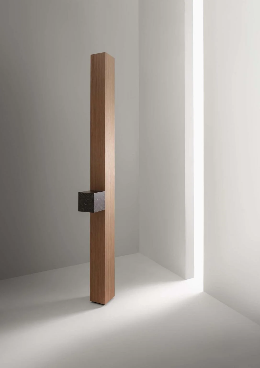Minimalist interior with a tall wooden post and a metal cube attached in a white room with a narrow vertical light opening.