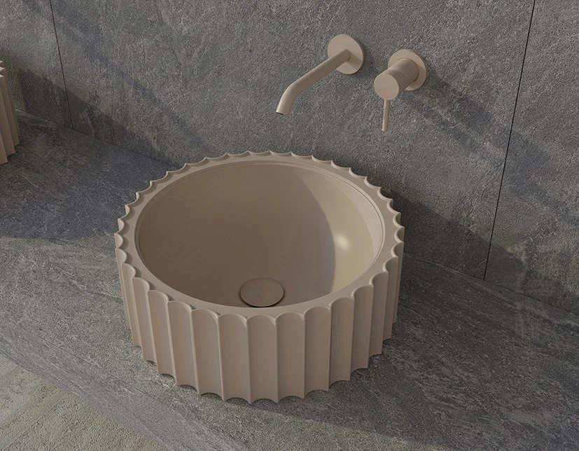 A modern installation of a round, beige sink with a ridged exterior, mounted on a gray stone wall with a matching wall-mounted faucet.