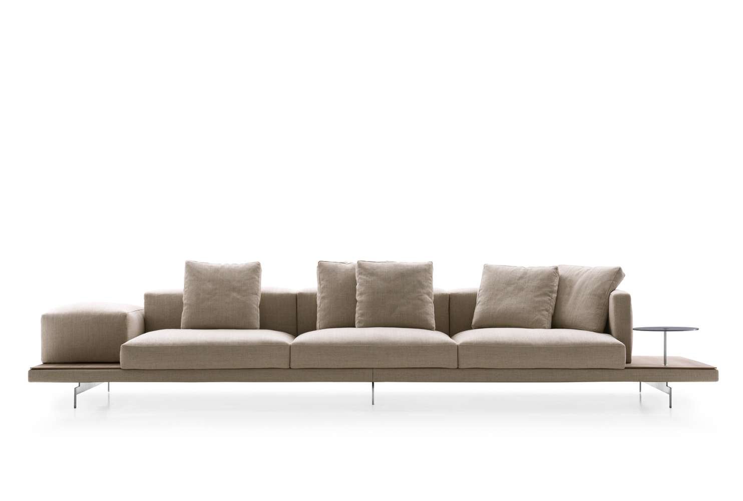 Beige fabric sofa with five cushions and a small round side table on the right against a white background.