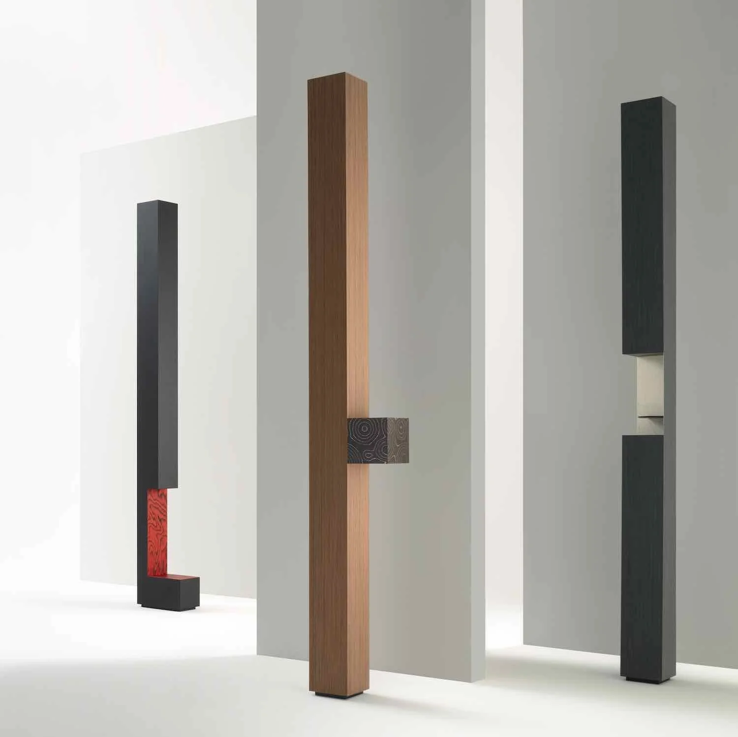 Three modern sculptures made of tall, rectangular wooden and metal blocks in an art gallery.