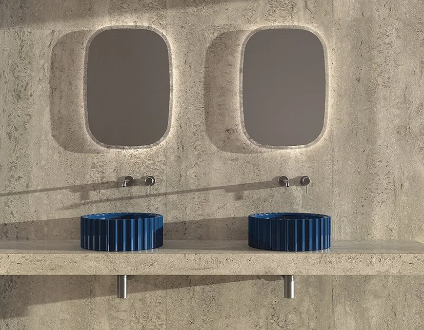 Modern bathroom with two oval mirrors, two blue vessel sinks, and wall-mounted faucets on a concrete wall