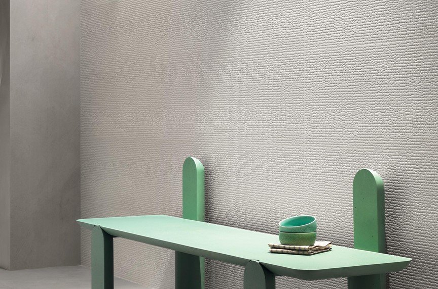 Minimalist mint green bench with two matching bowls and a striped cloth on top, against a textured light gray wall.