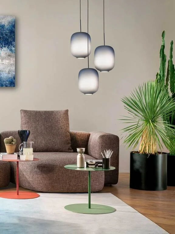 Living room with a brown sofa, three hanging pendant lights, a large potted palm plant, and two side tables with decorative items