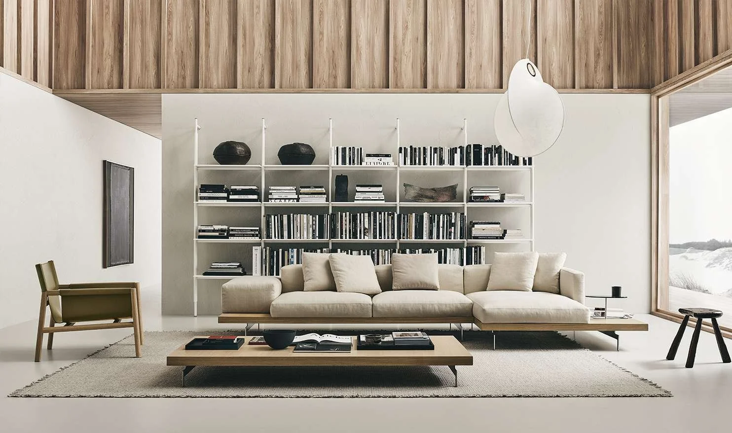 Minimalist living room with cream sofa, wooden coffee table, white wall bookshelf filled with black and white books, wood-paneled ceiling, large window showing outdoor landscape
