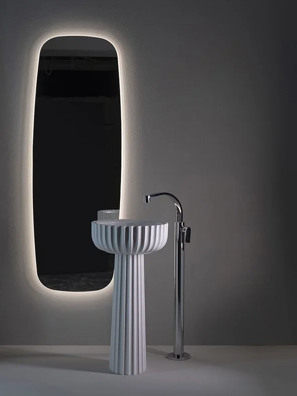 Modern bathroom with a white fluted pedestal sink, a tall mirror with backlit lighting, and a chrome faucet on a dark gray wall.
