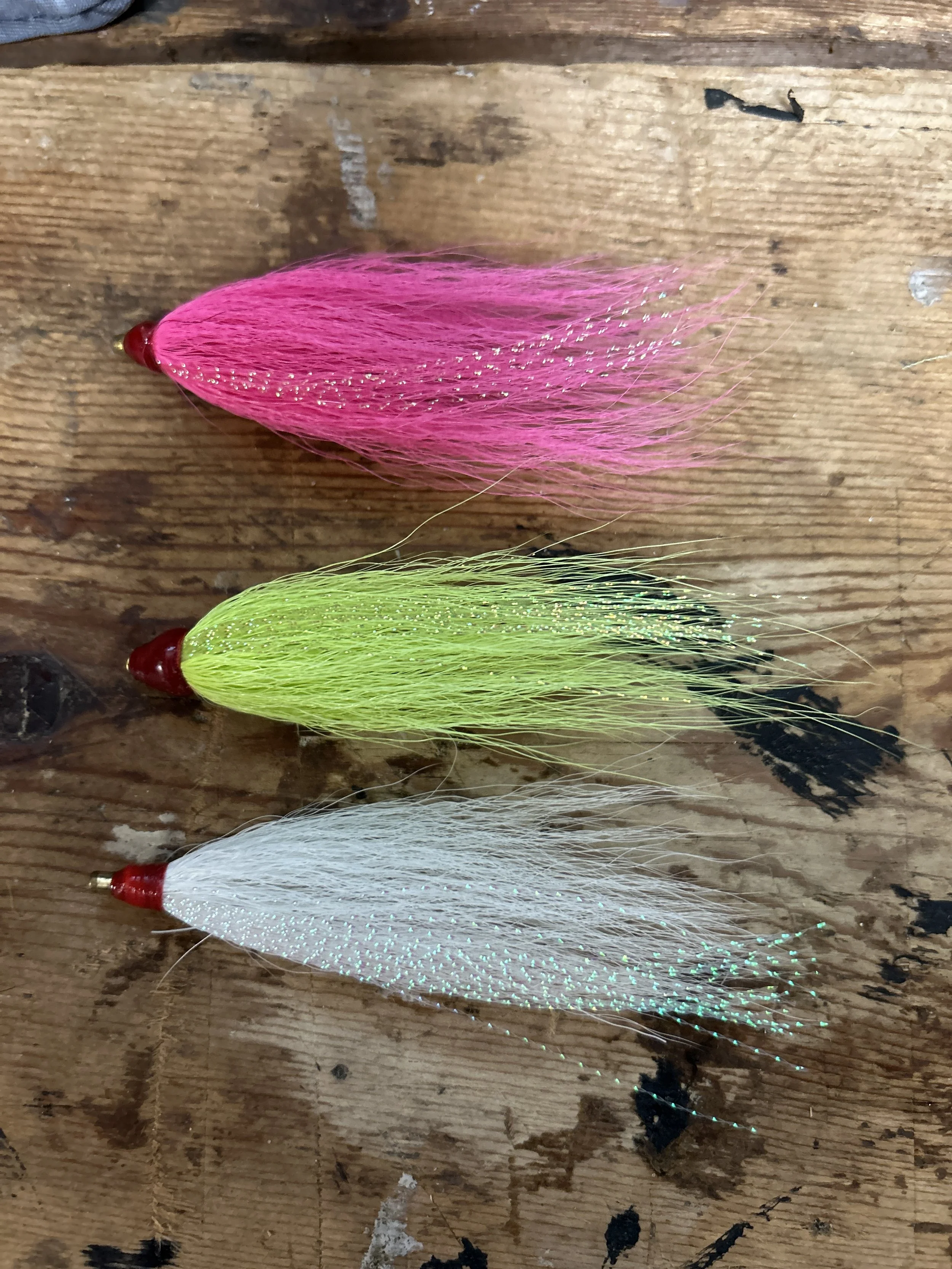 Several fishing lures with pink, green, and white colors lying on a weathered wooden surface. sandbar Captain Tilly OC Fishing Charters. Ocean City, MD