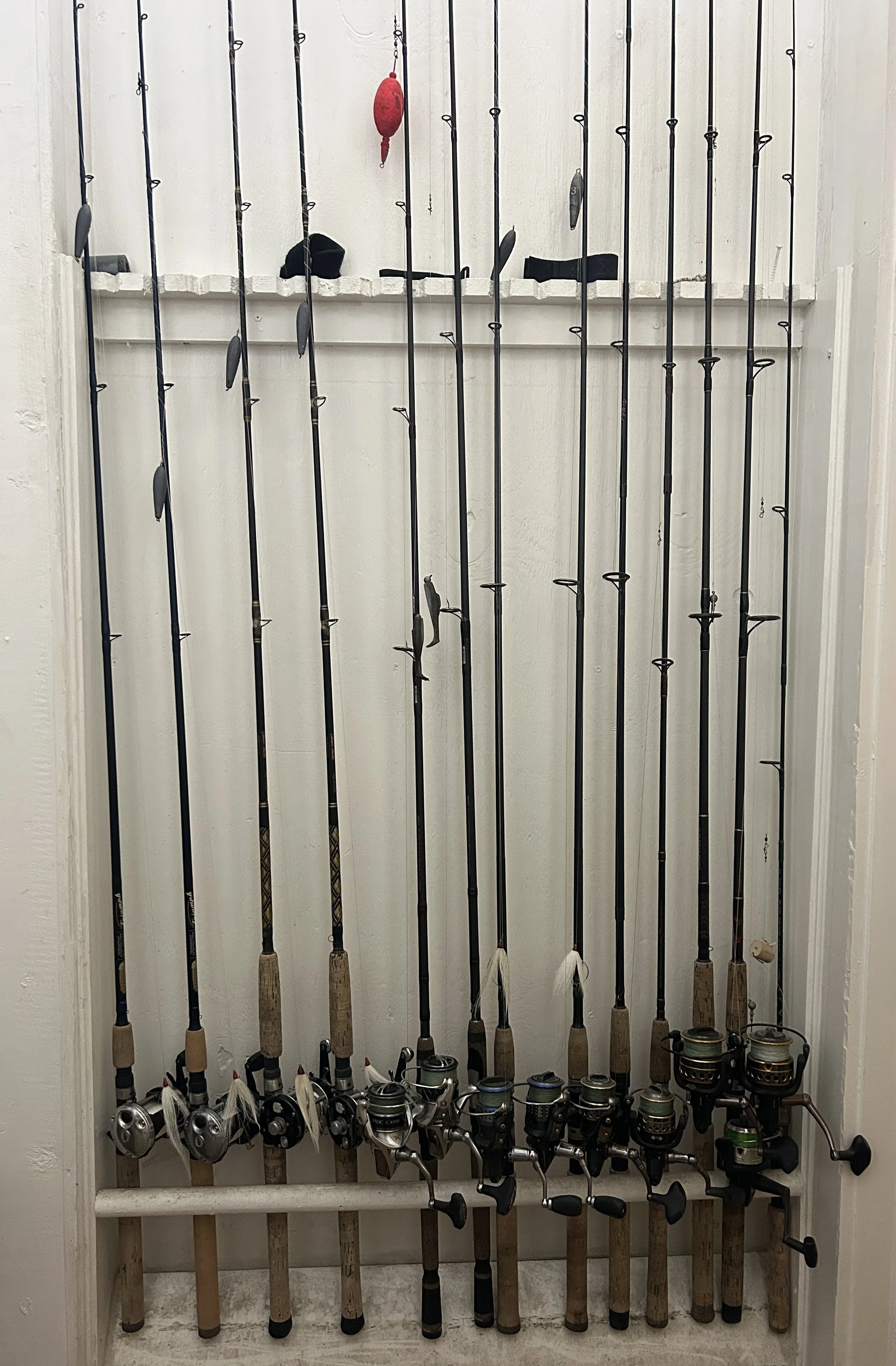 A collection of fishing rods with reels, lined up and leaning against a white painted wall with a small shelf above them.
Captain Tilly OC fishing charters. Ocean City, MD.