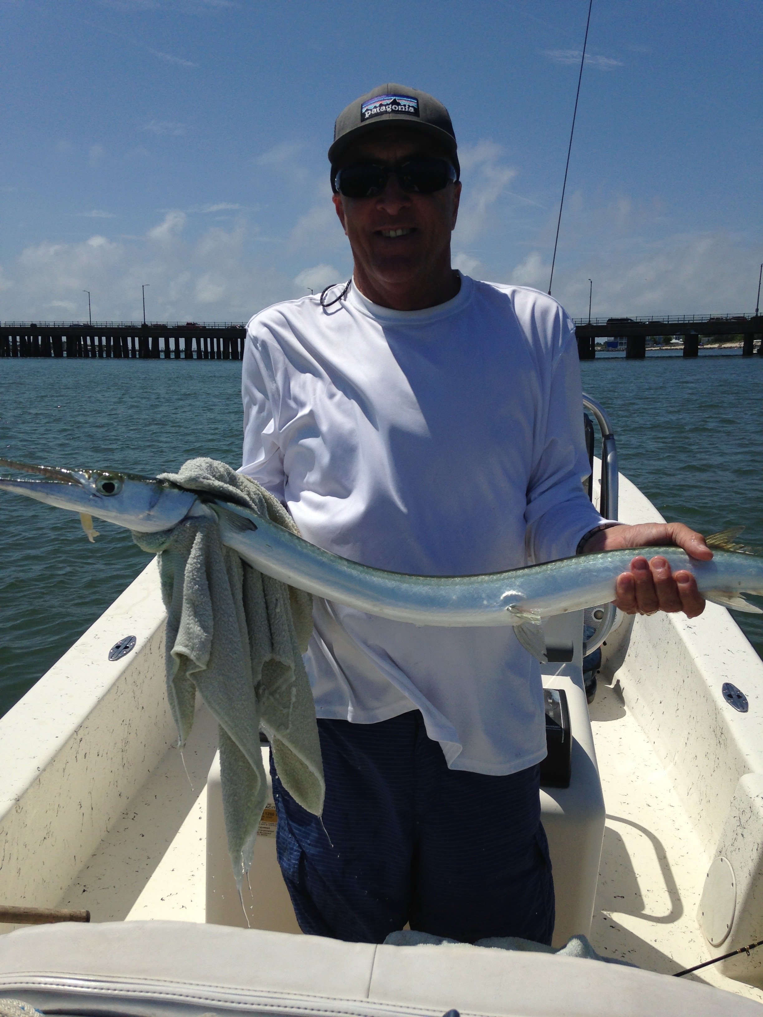 A man holding a fish on a boat with a bridge and blue sky in the background. sandbar Captain Tilly OC Fishing Charters. Ocean City, MD