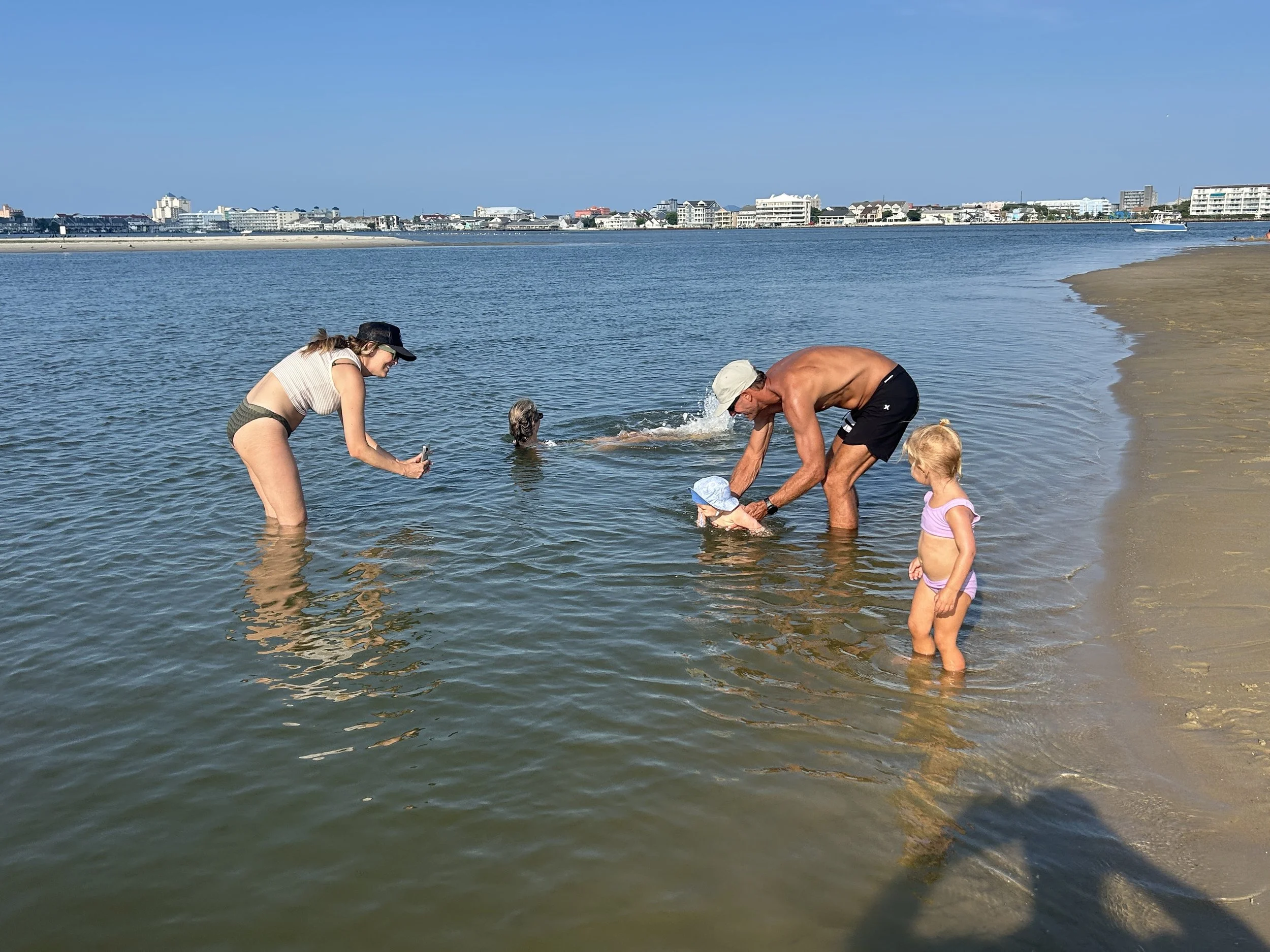 People wading in shallow water at a beach with a cityscape in the background. sandbar Captain Tilly OC Fishing Charters. Ocean City, MD