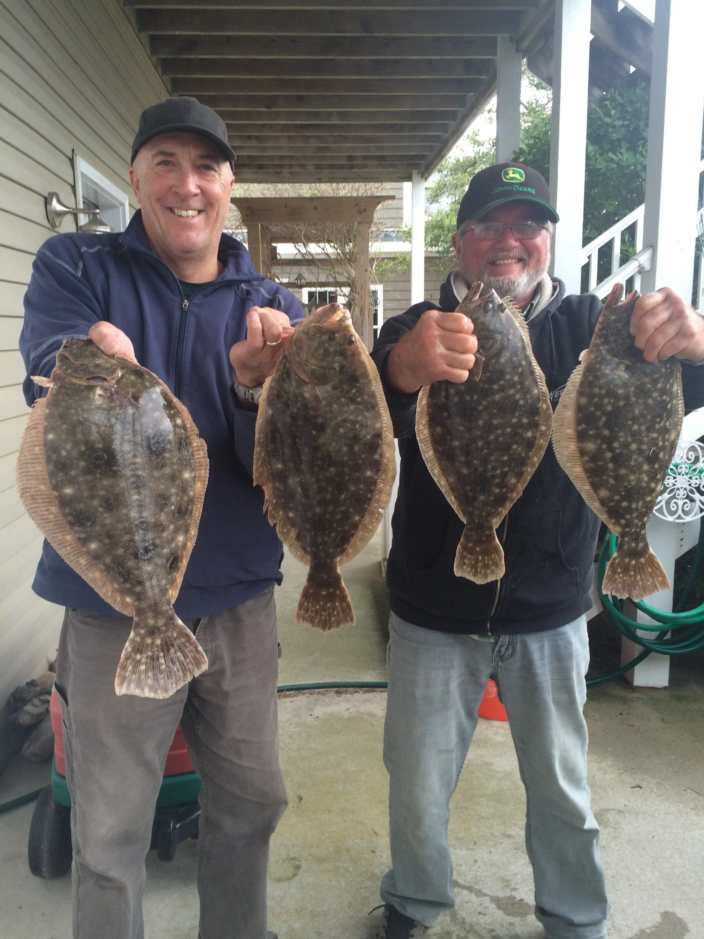 Two men standing outdoors holding large flat fish they caught, smiling at the camera.