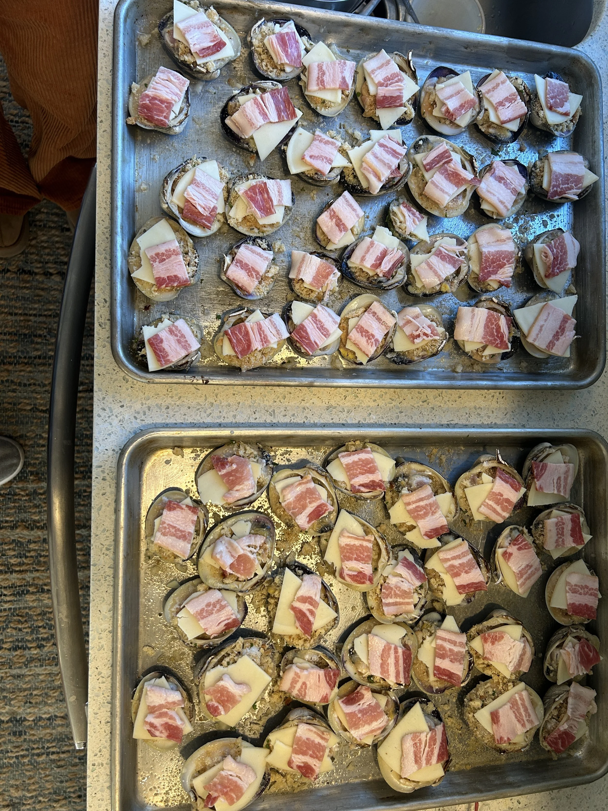 A metal tray filled with cooked clams casino topped with melting cheese and strips of bacon. sandbar Captain Tilly OC Fishing Charters. Ocean City, MD