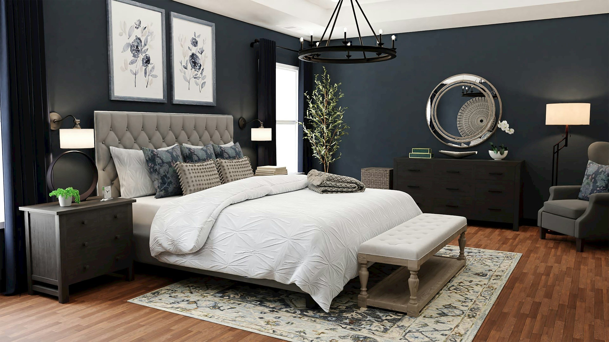 A modern bedroom with dark blue walls, a beige tufted headboard, and a white comforter. Decor includes framed botanical art, potted plants, a mirror, and lamps. There is a bench at the foot of the bed, a dark dresser, and a sitting area with an armchair and floor lamp. A patterned area rug is on the hardwood floor.