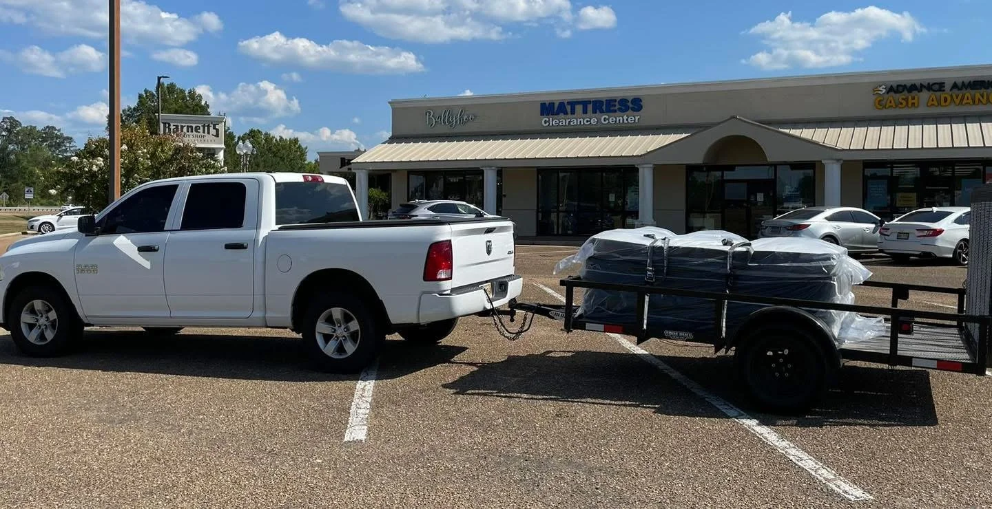 A white pickup truck towing a trailer with wrapped furniture in a parking lot.
