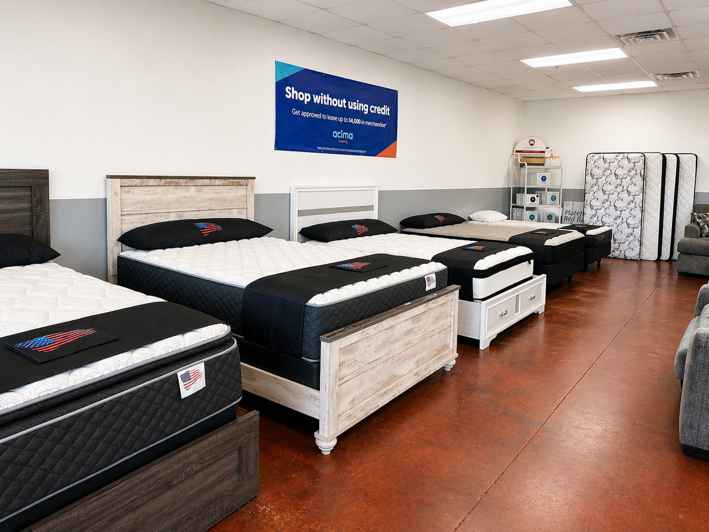Display of multiple mattresses and beds in a store showroom, with some mattresses stacked and others laid out for display.