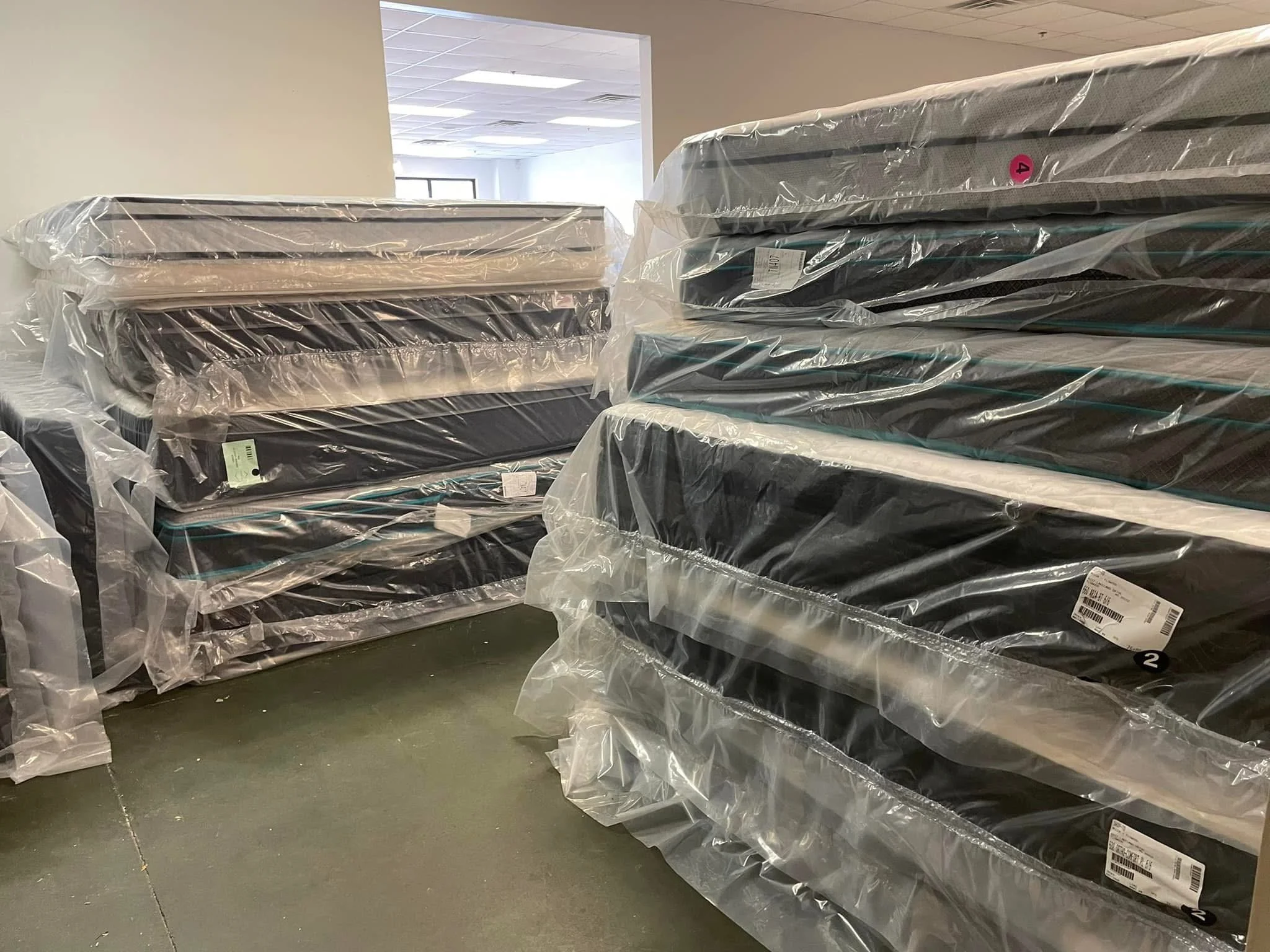 Stacks of new mattresses wrapped in plastic, stored in a warehouse or showroom.