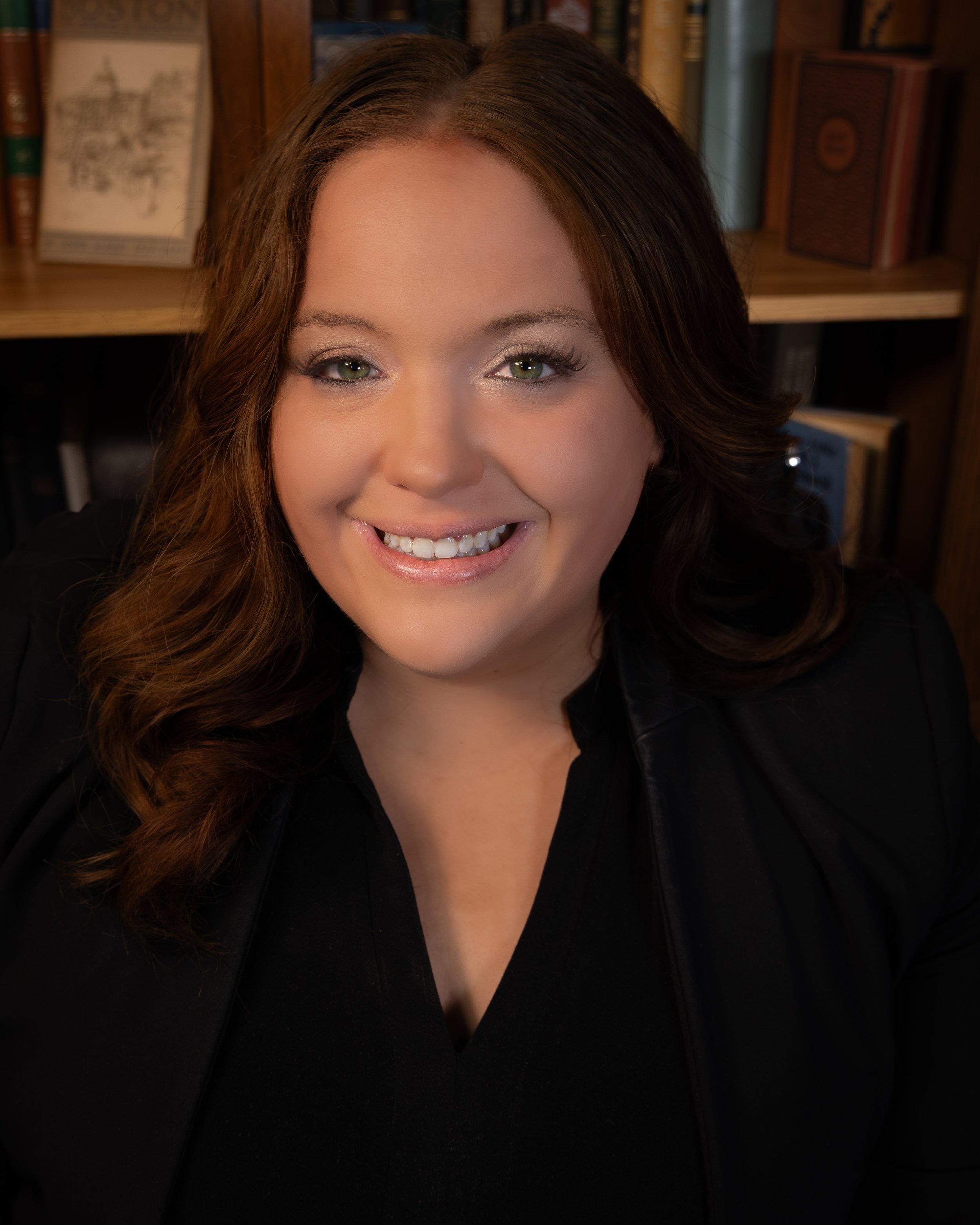 Close-up of a woman with brown hair, smiling, with a background of bookshelves filled with books.