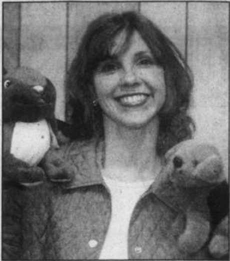 A woman smiling, holding two plush toy animals, a bear and a frog.