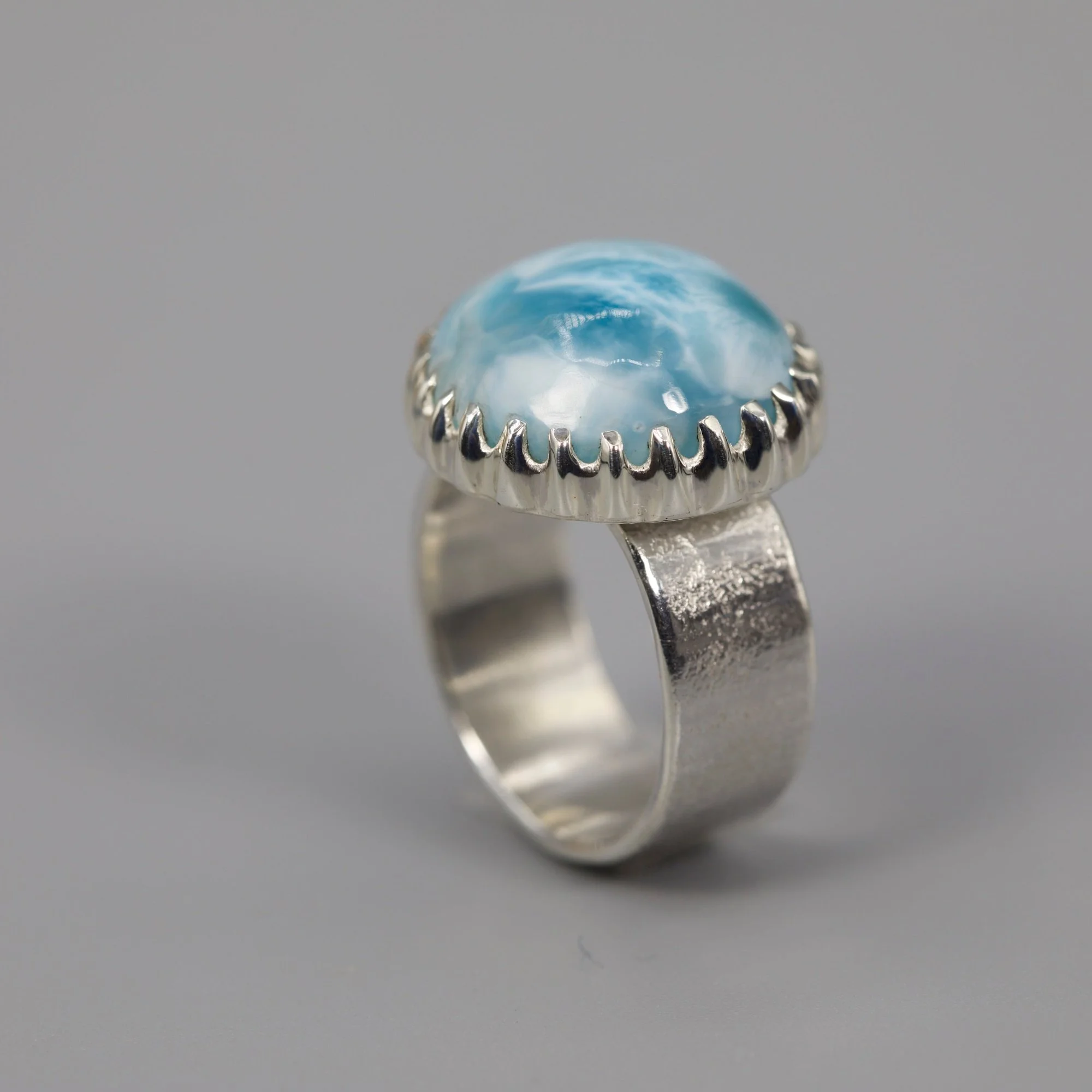 A silver ring with a large, round, cabochon blue gemstone set in a prong setting.
