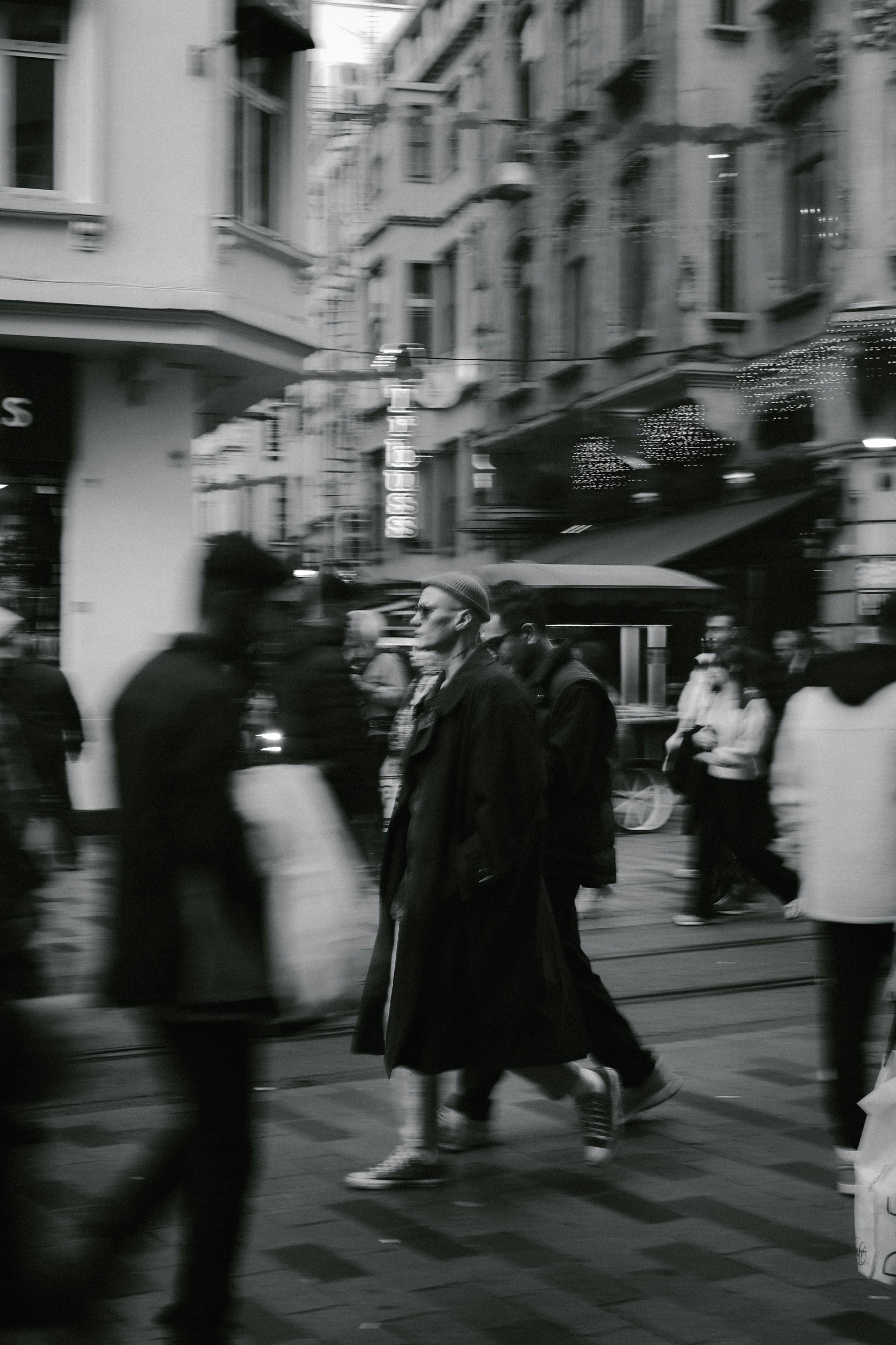 Man in a coat and beanie walking through a busy, blurred crowd