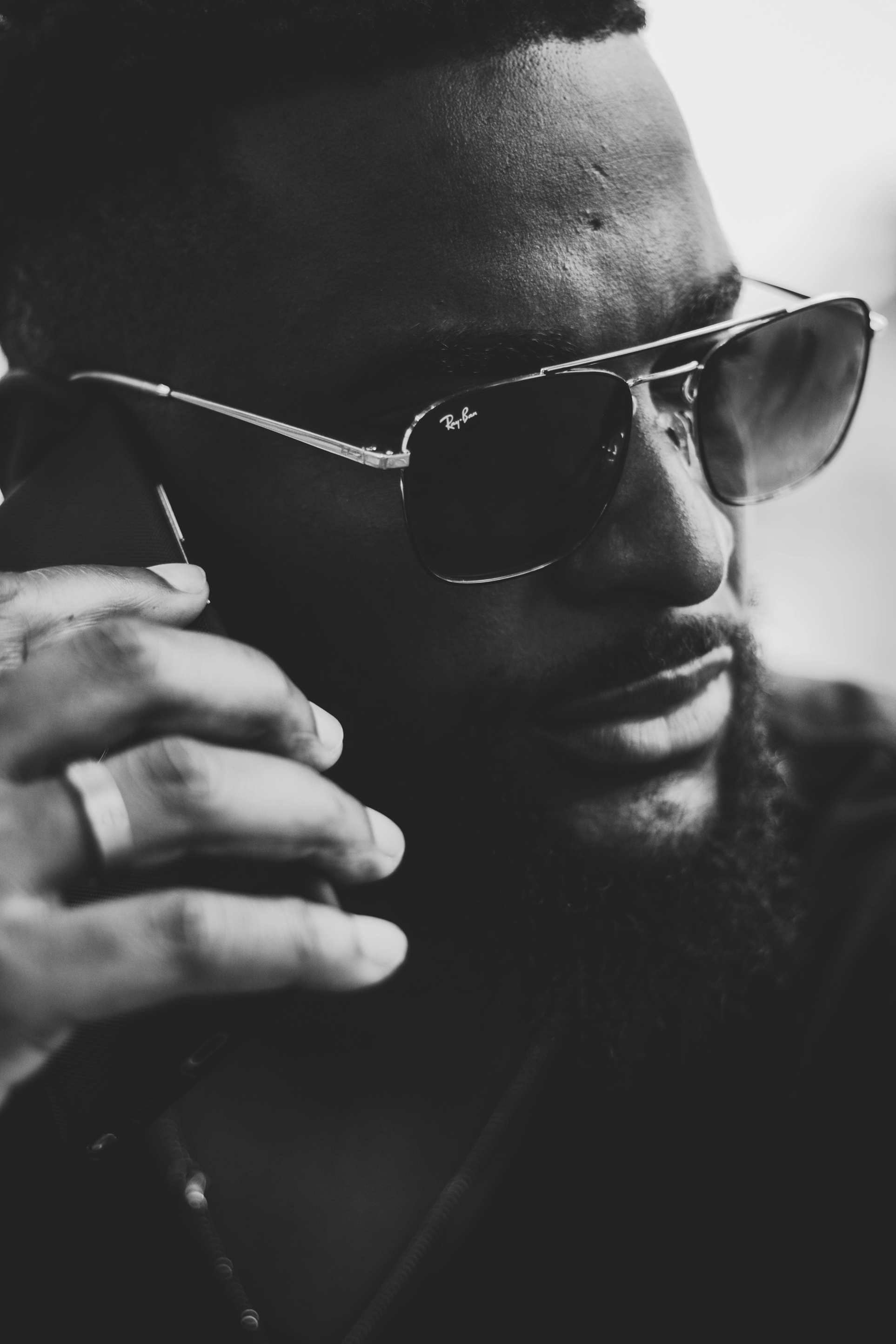 Close-up black and white photo of a man wearing sunglasses, holding a phone to his ear, with only part of his face visible.