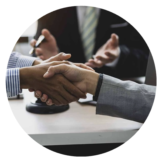 Two people shaking hands at a business meeting, with a third person in the background taking notes.