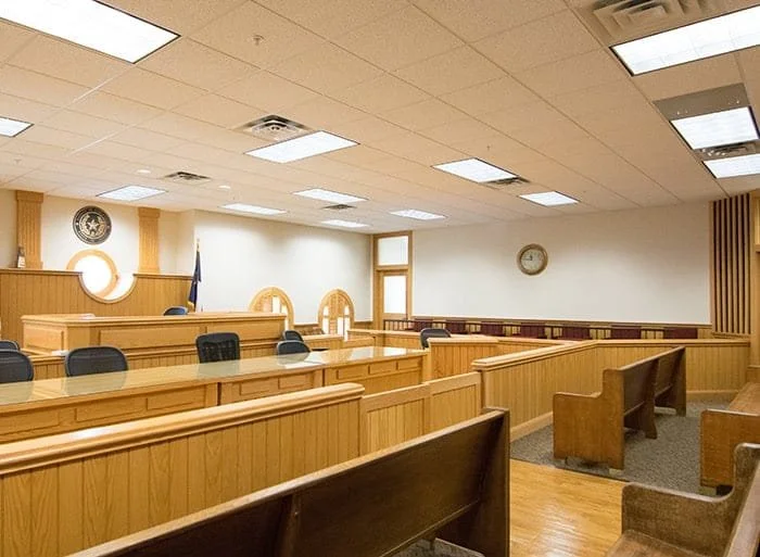 Empty courtroom with wooden benches, a judge's bench, and a flag in the background.