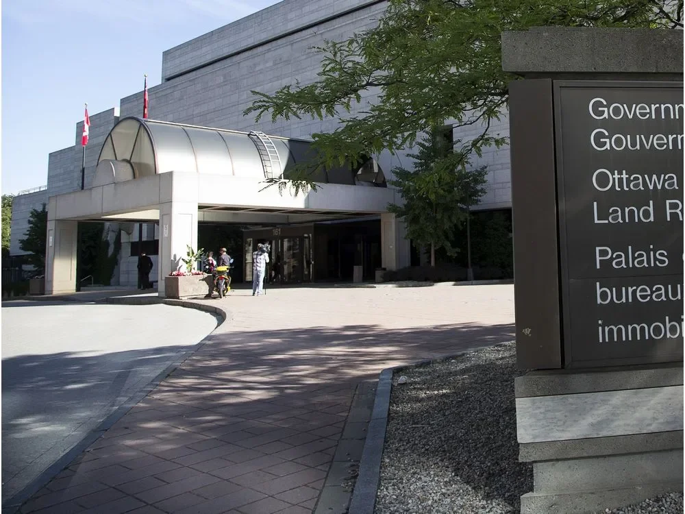 The exterior of a government building with flags, people standing near the entrance, and a sign indicating it is the Ottawa Land Registry Office.