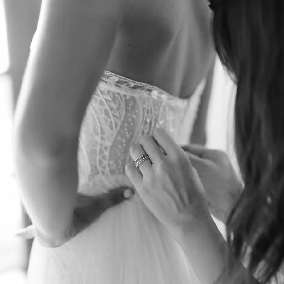 Persona ajustando un vestido de novia con encaje y detalles delicados.