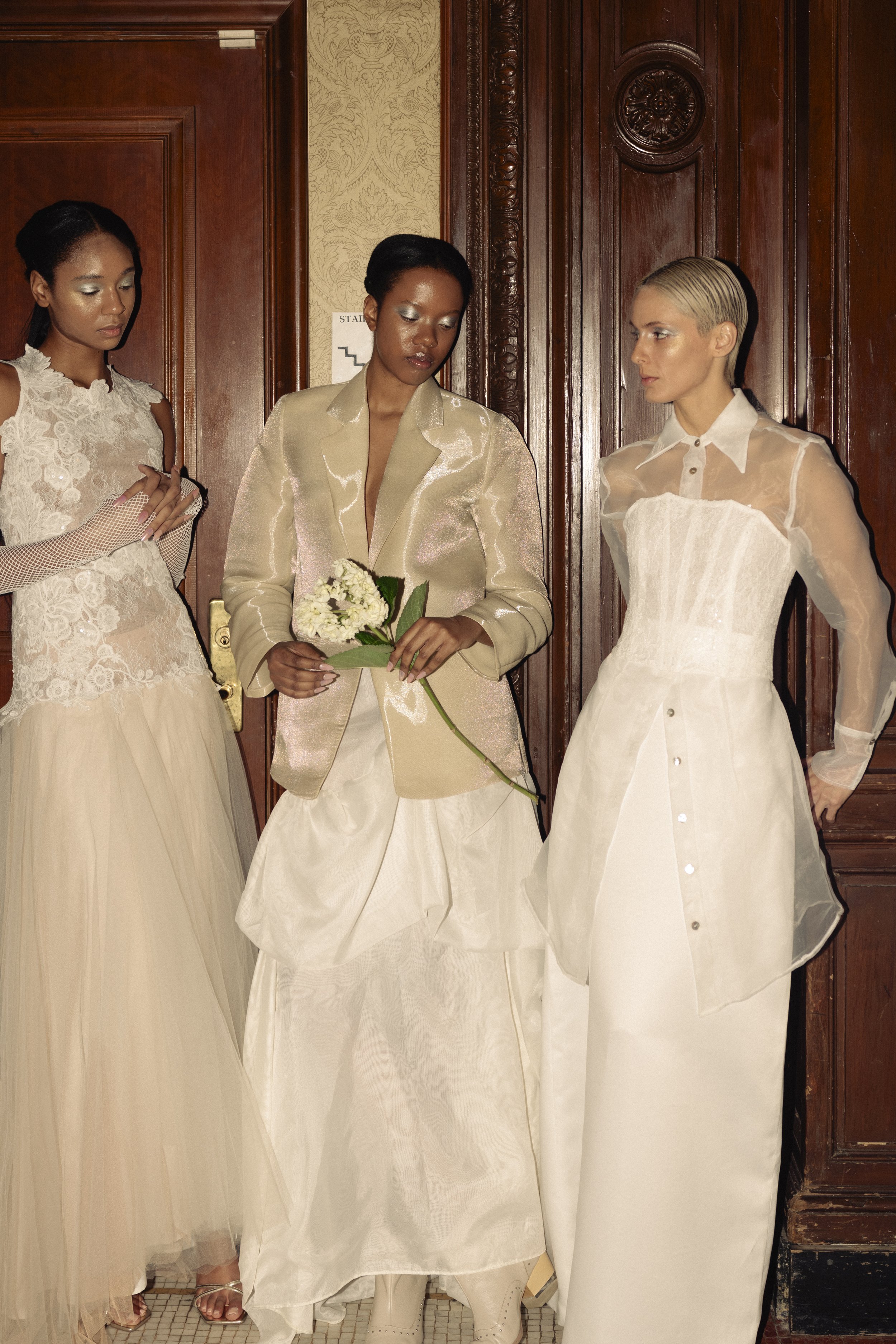 Tres modelos femeninas con vestidos de novia en una sesión de fotos de moda nupcial, momentos antes de salir a la pasarela.