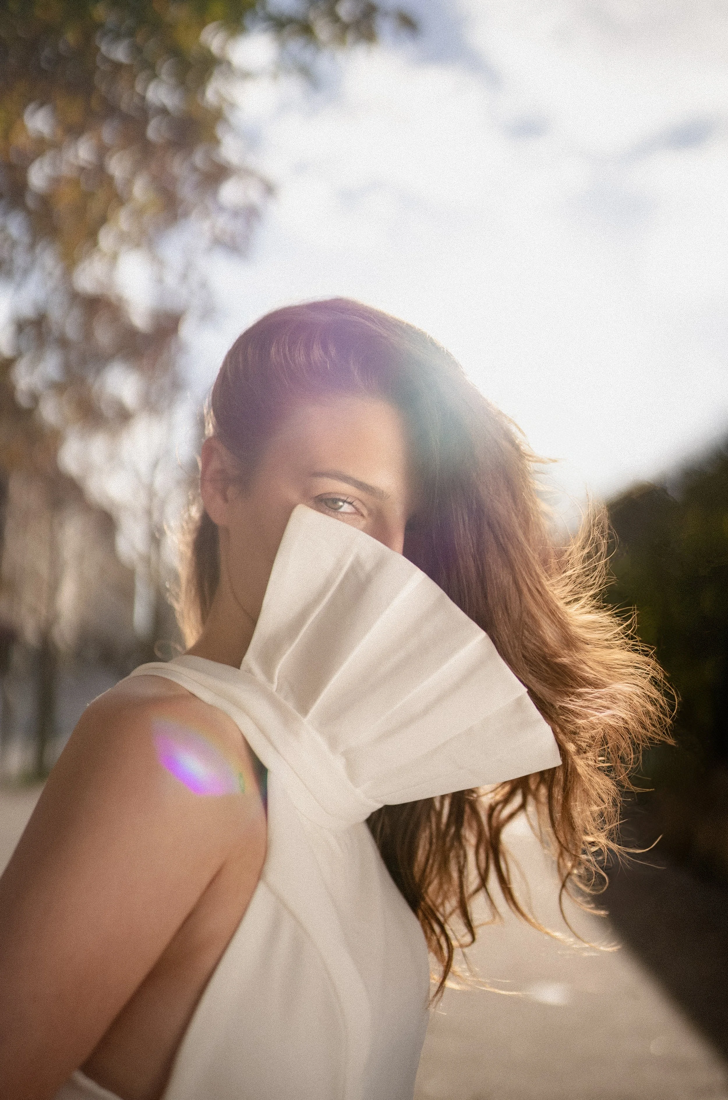 Mujer con cabello rizado y largo usando vestido blanco CON CUELLO EN FORMA DE ABANICO al atardecer con luz solar.