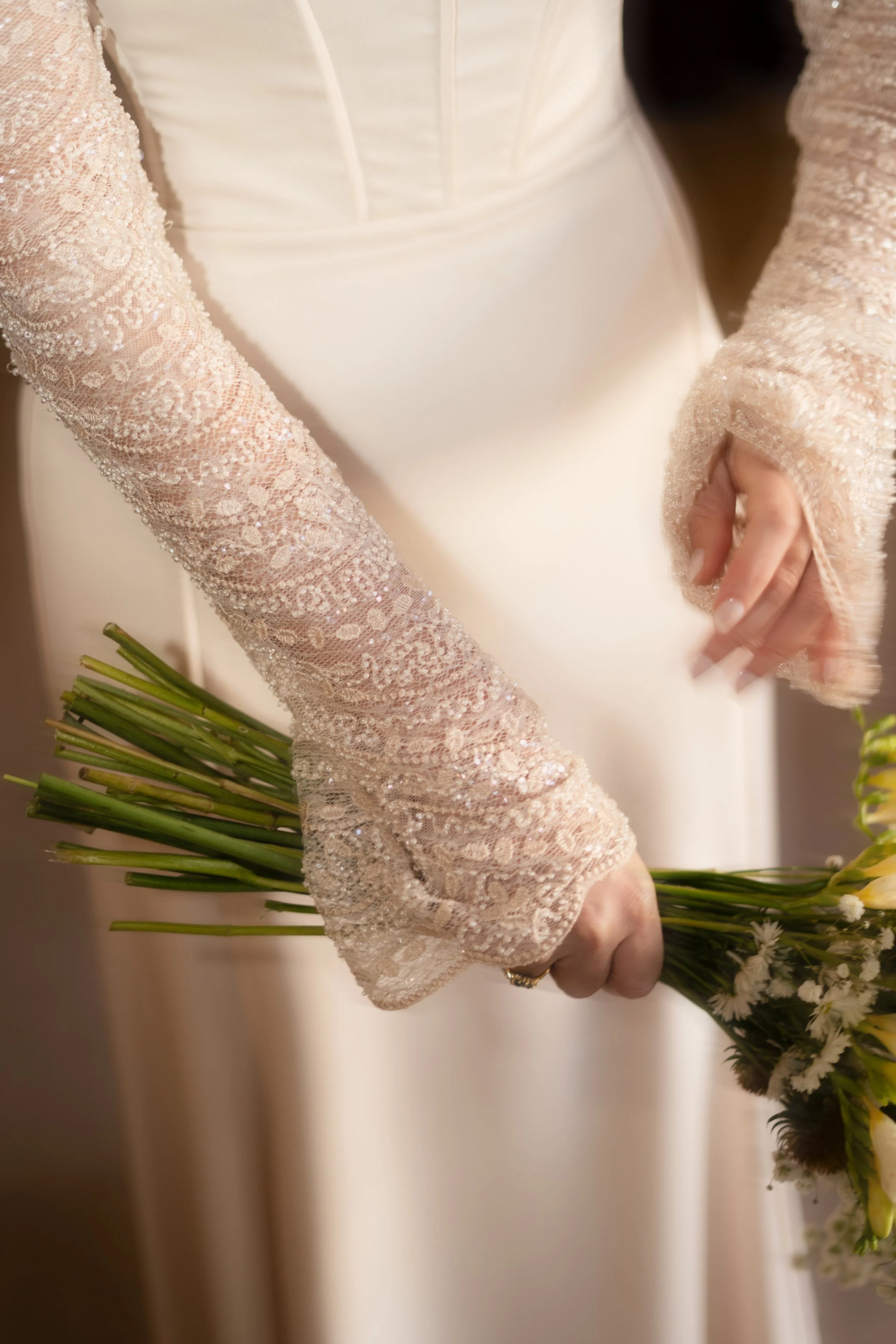 Manos de una novia con guantes de encaje sosteniendo un ramo de flores blancas y verdes. Vestido de Ofelia Otello. Fotografía de Nath Planás.