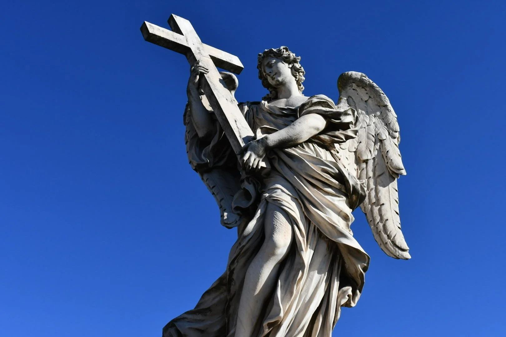Statue of an angel holding a cross against a blue sky.
