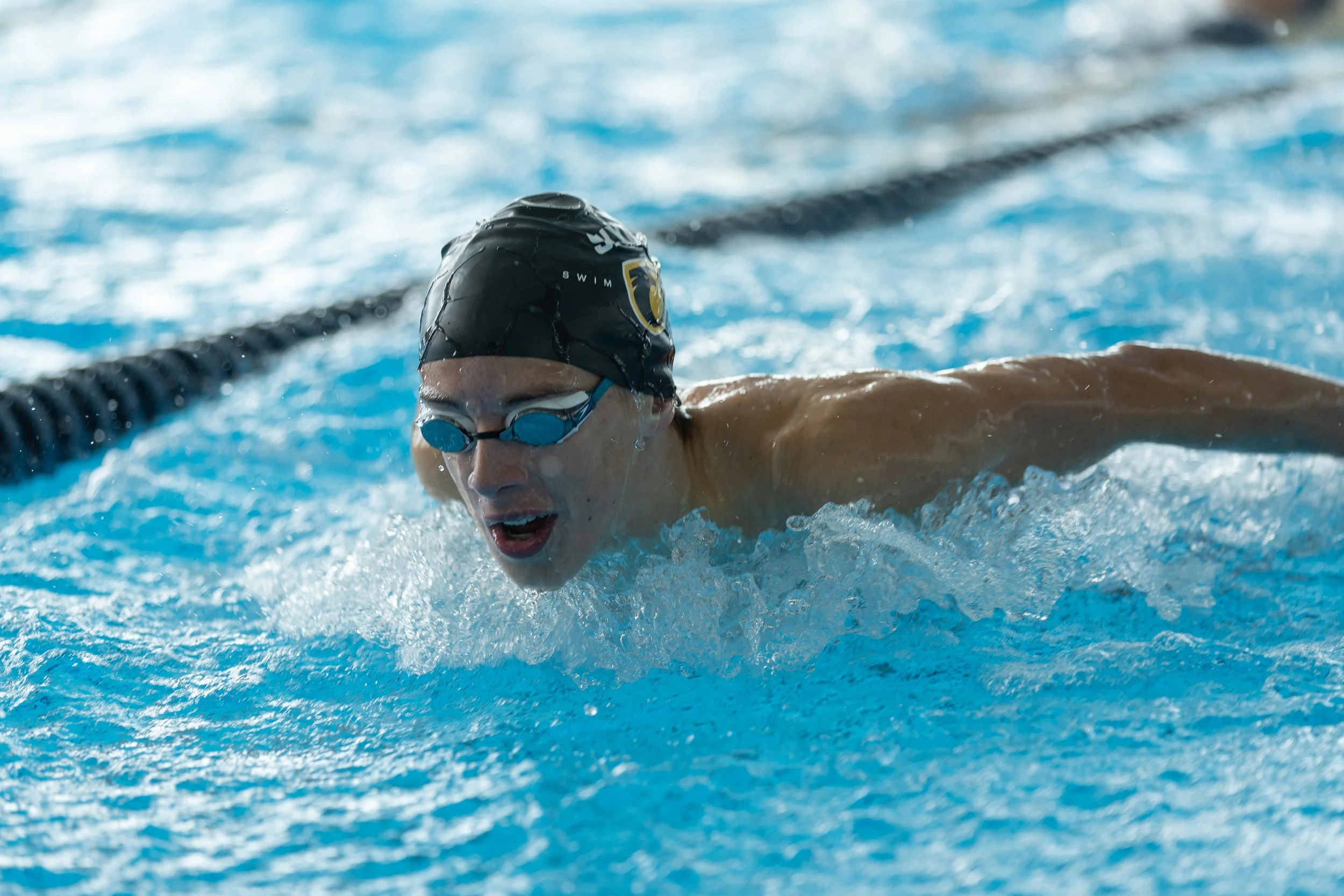 A swimmer wearing a black swim cap and goggles, swimming in a pool.