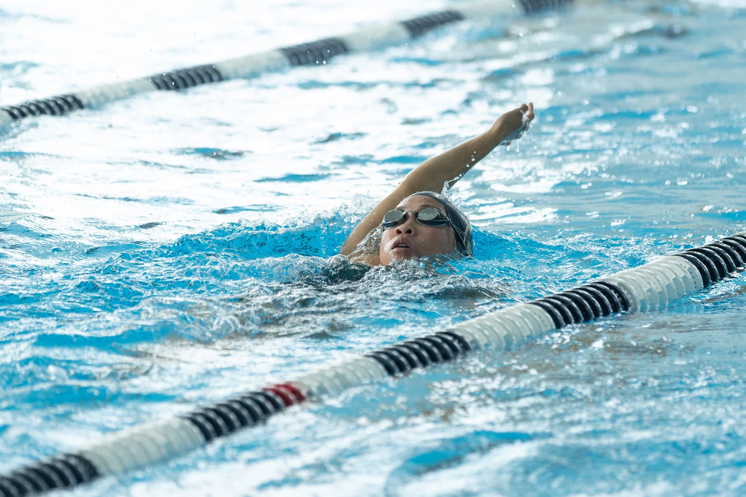 Swimmer wearing goggles and swim cap, swimming in a lane of an indoor swimming pool.