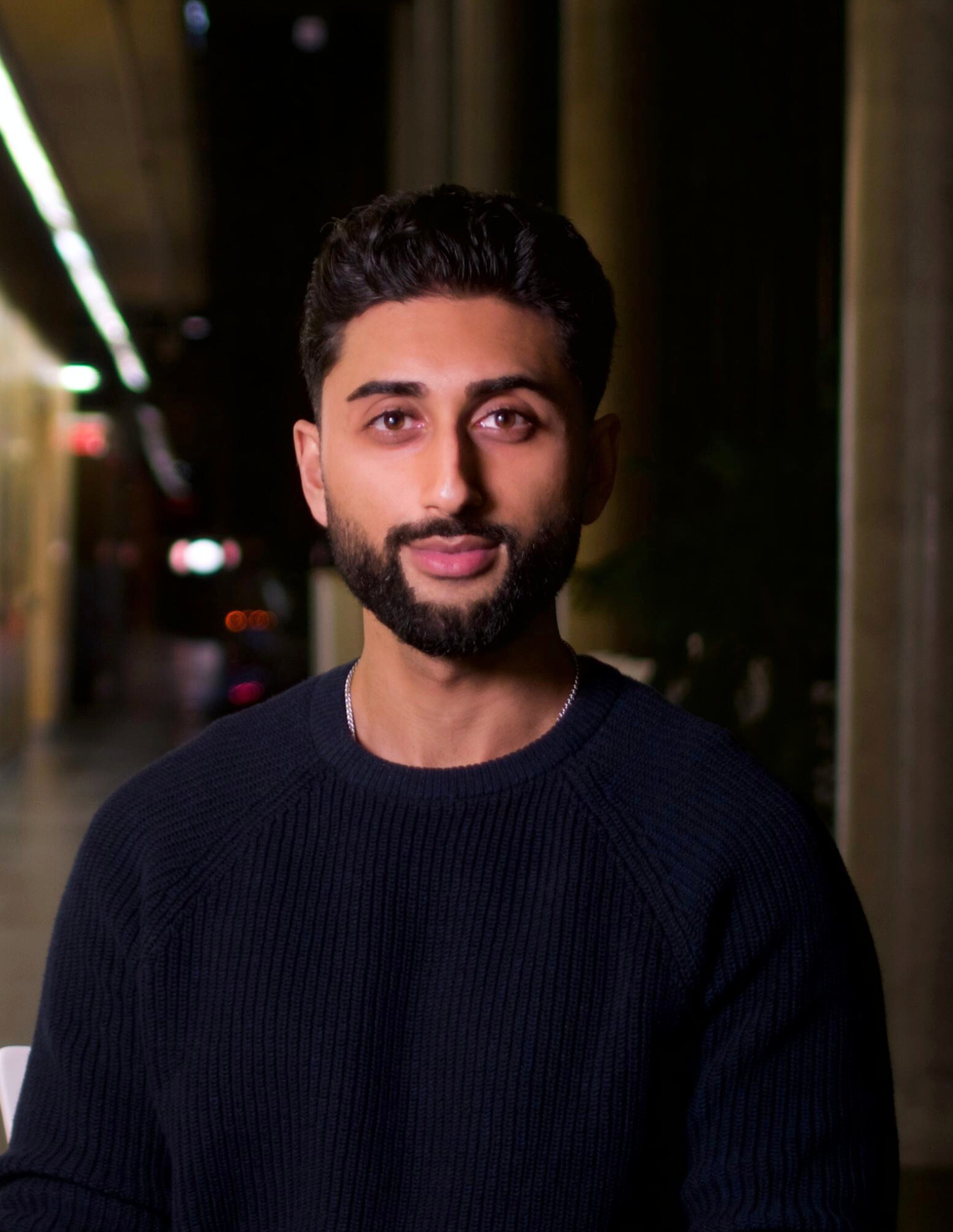 Head shot of Muhib Mansuri, founder & CEO of SwiftApprove and founding member of BDE Group. He is wearing a black sweater, standing in an indoor hallway with blurred lights in the background.