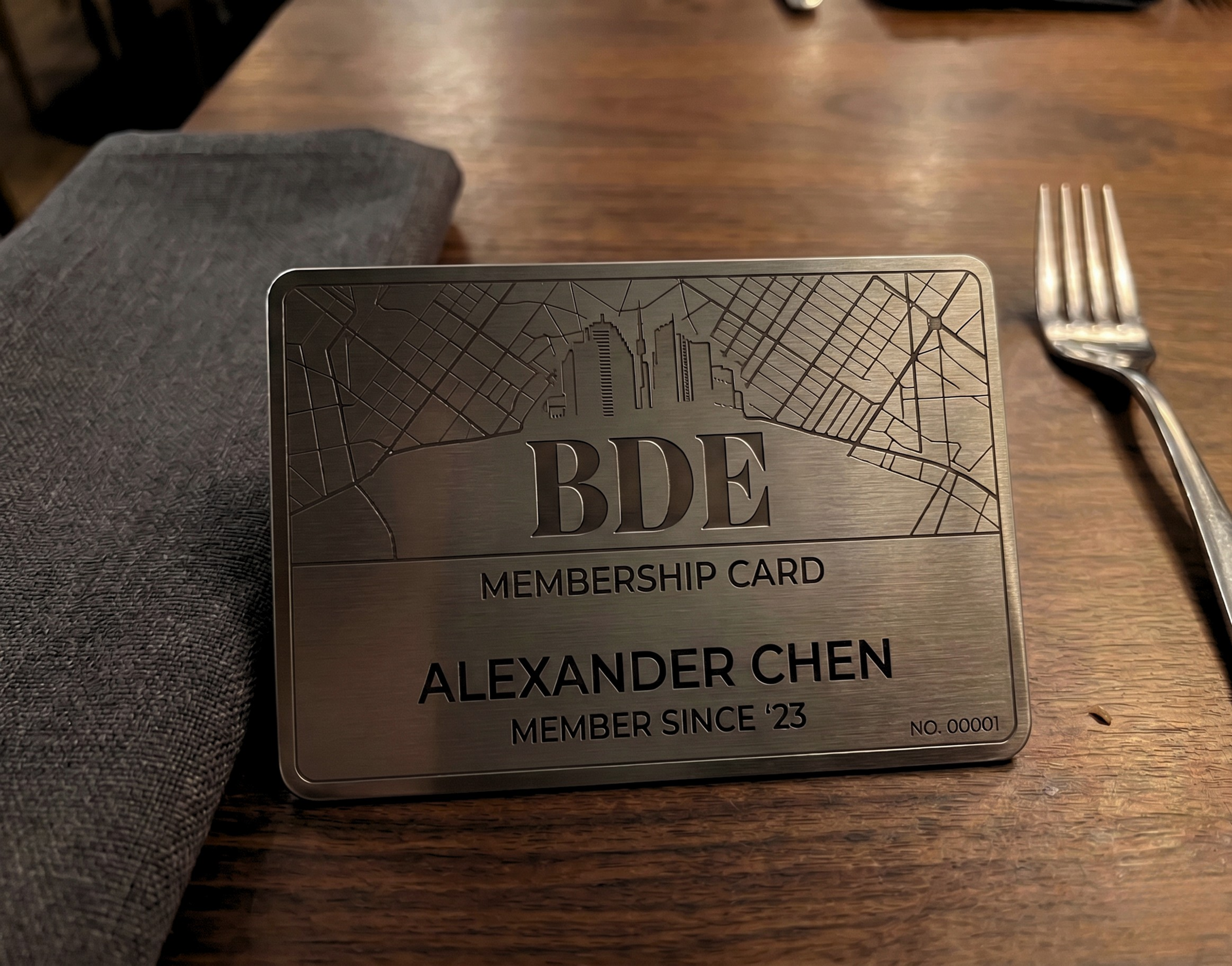 A BDE Group membership card on a wooden table with a fork and a cloth napkin nearby.