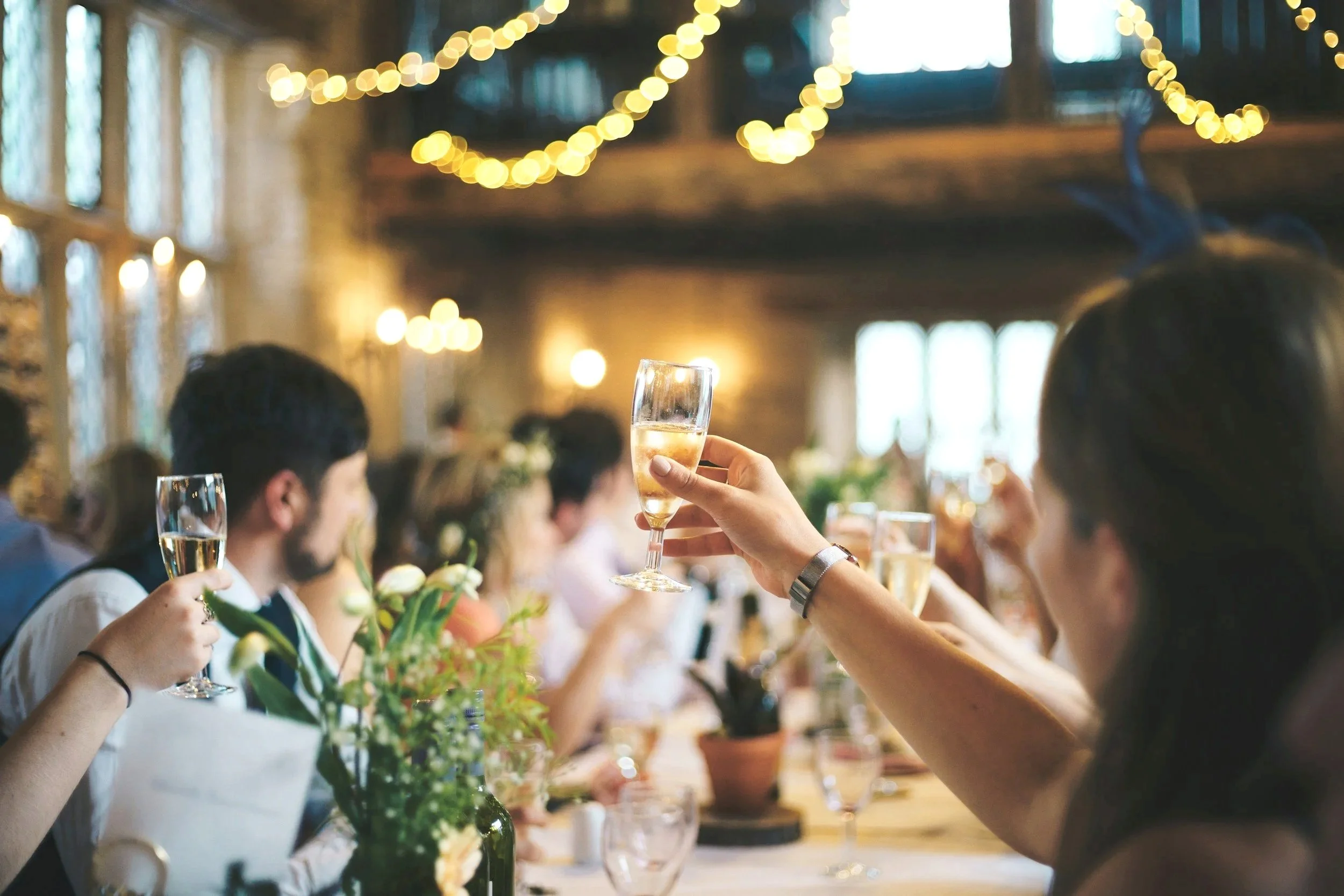 People at a celebration or wedding raising glasses of champagne for a toast in a warmly lit decorated venue.