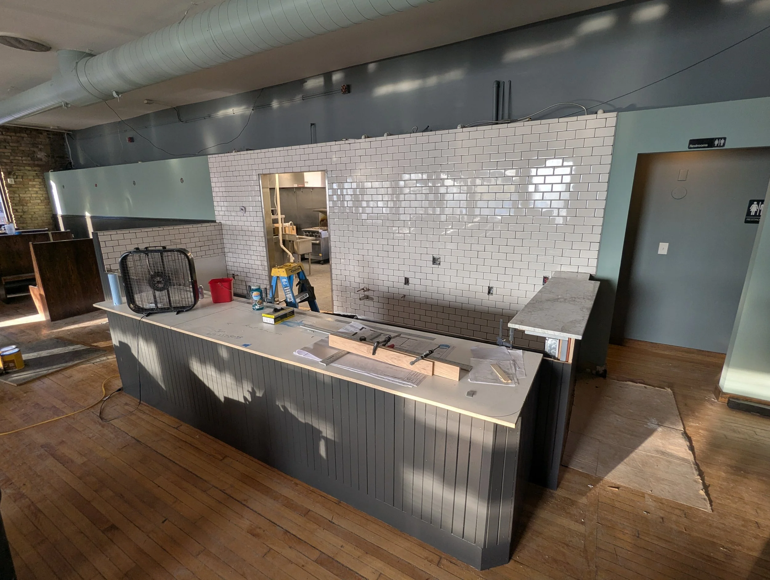 Interior of a restaurant under renovation with a countertop, construction tools, and a kitchen area in the background.