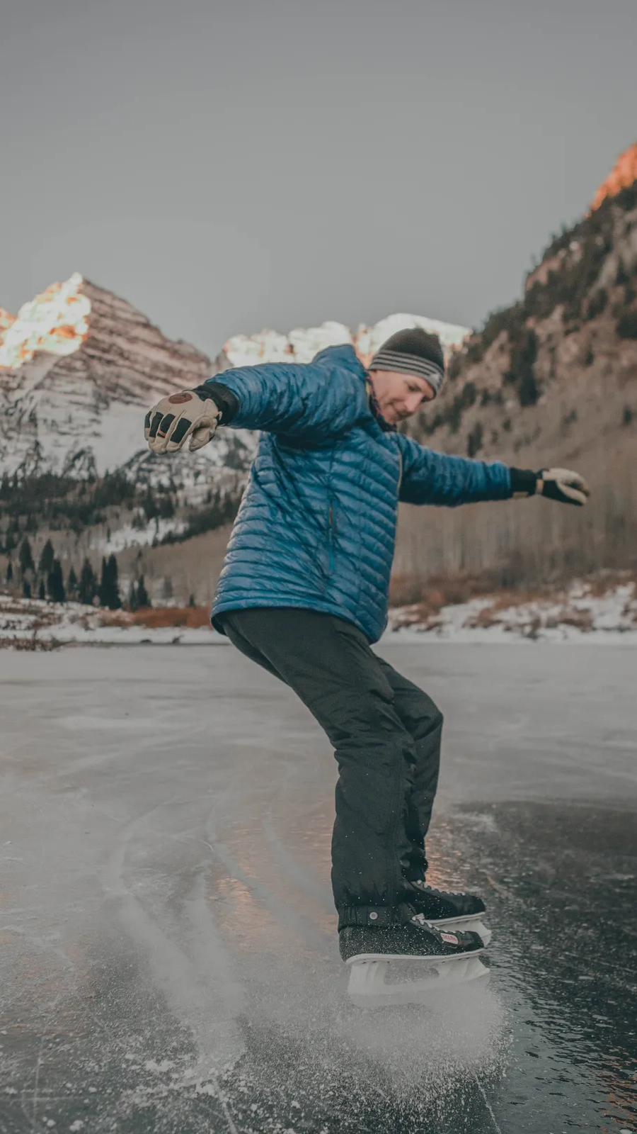 Dr. Jon Kedrowski ice skating on a frozen lake in Colorado with snow-covered mountains in the background.