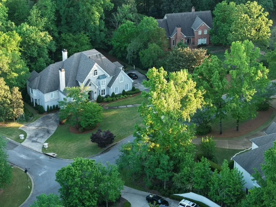 Aerial view of a large suburban home with a curved driveway, surrounded by lush green trees and landscaped yard.