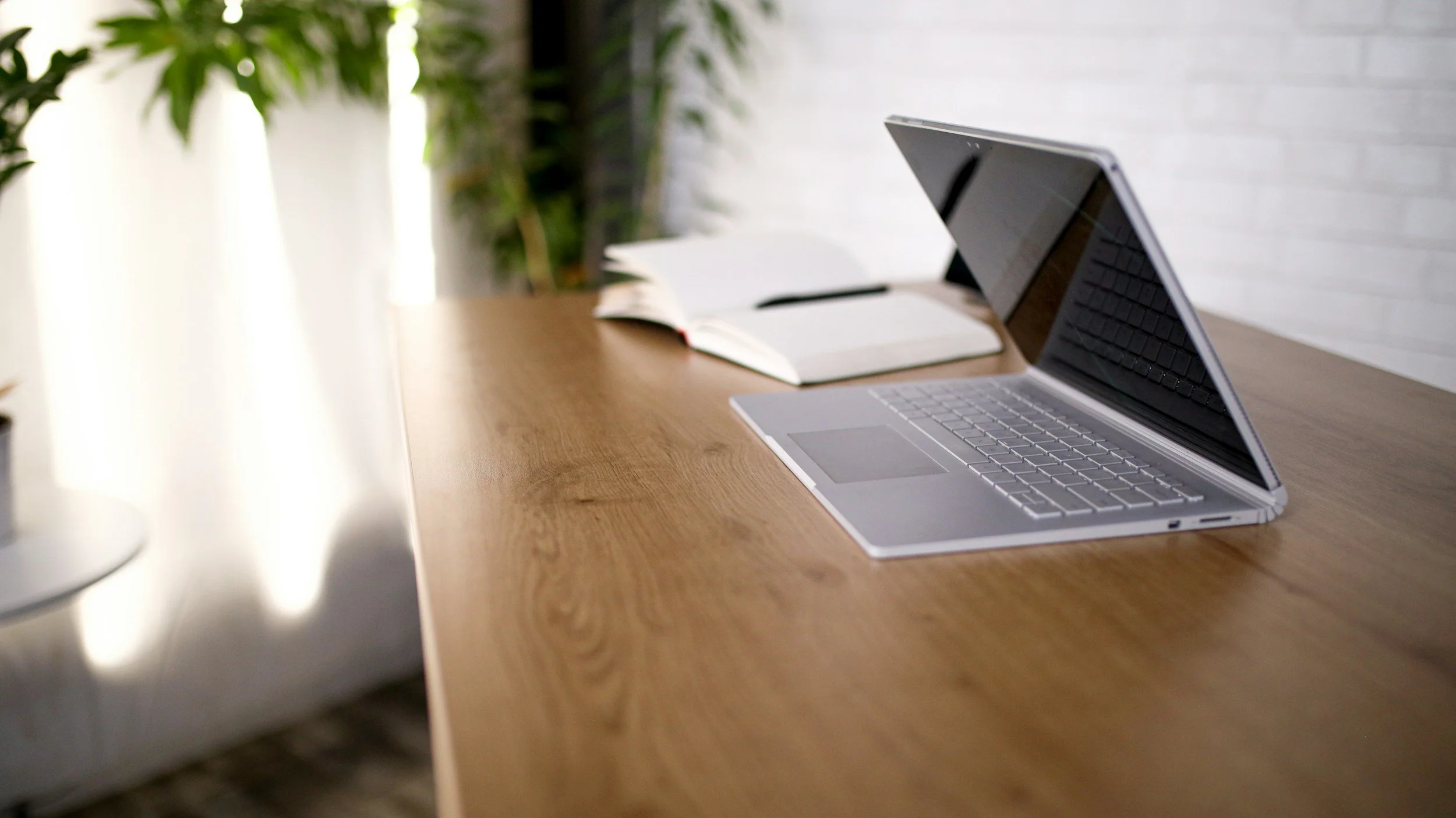 A desk setup featuring a white keyboard, a white mouse, a computer monitor displaying a yellow abstract pattern, a small yellow toy car, a white desk lamp to the right of the monitor, a white and yellow table lamp to the left of the keyboard, and a white cord on the right side of the desk against a yellow wall.