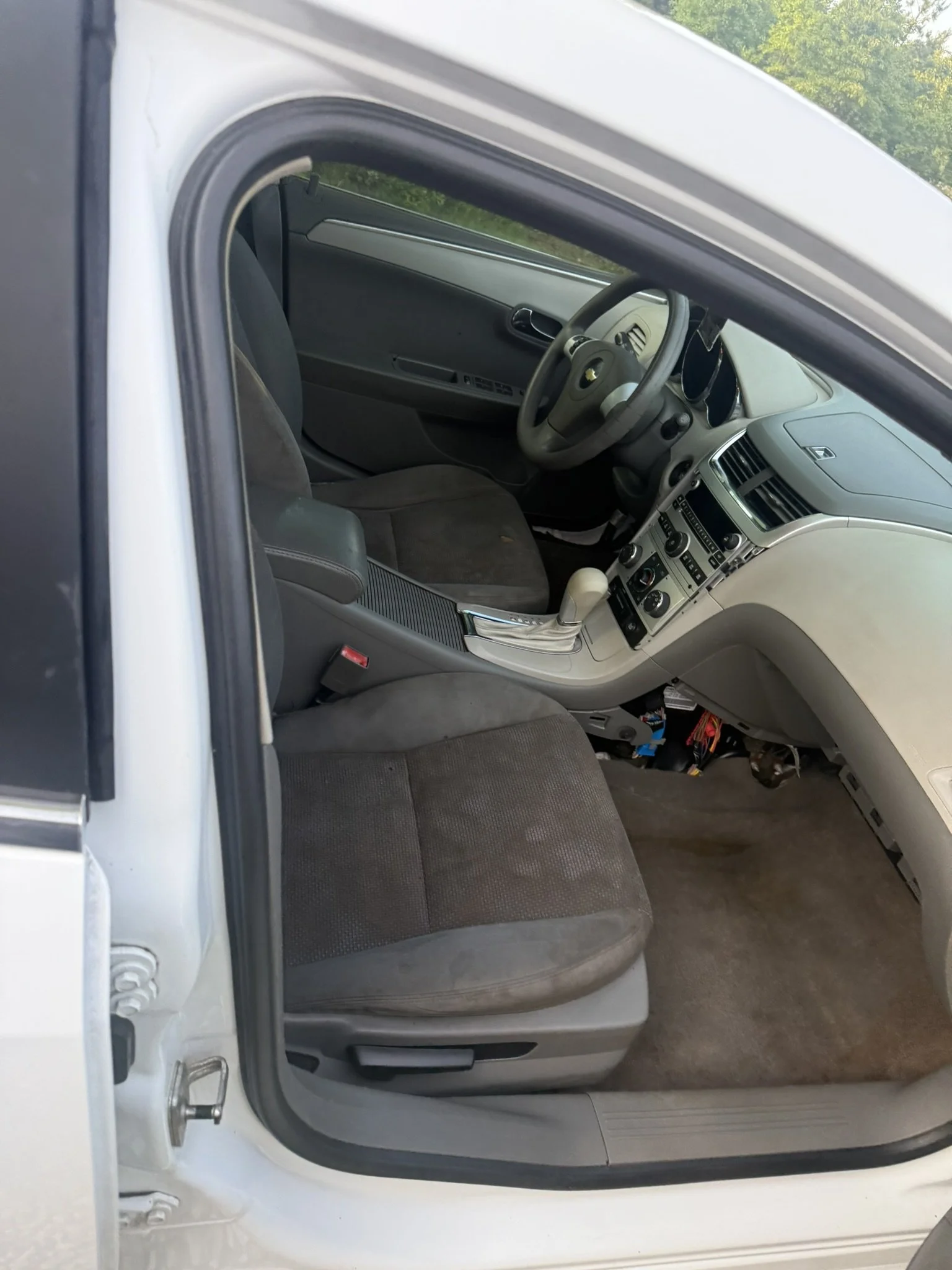 Interior of a car viewed from the open driver's side door showing the front seat, dashboard, steering wheel, and center console in a vehicle with a gray and black interior.