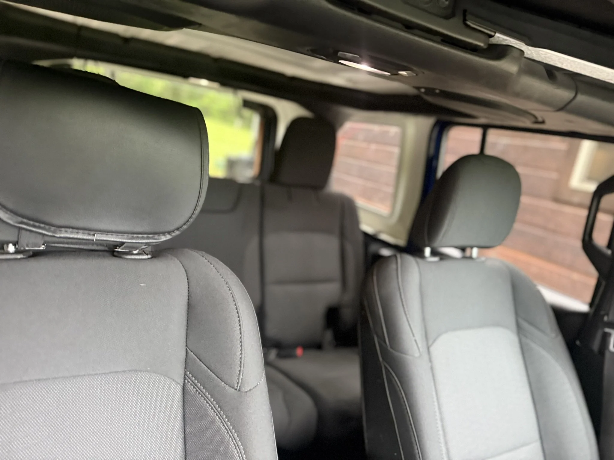 Inside a vehicle showing multiple rows of grey fabric-covered seats with headrests, viewed from the back seat looking towards the front.