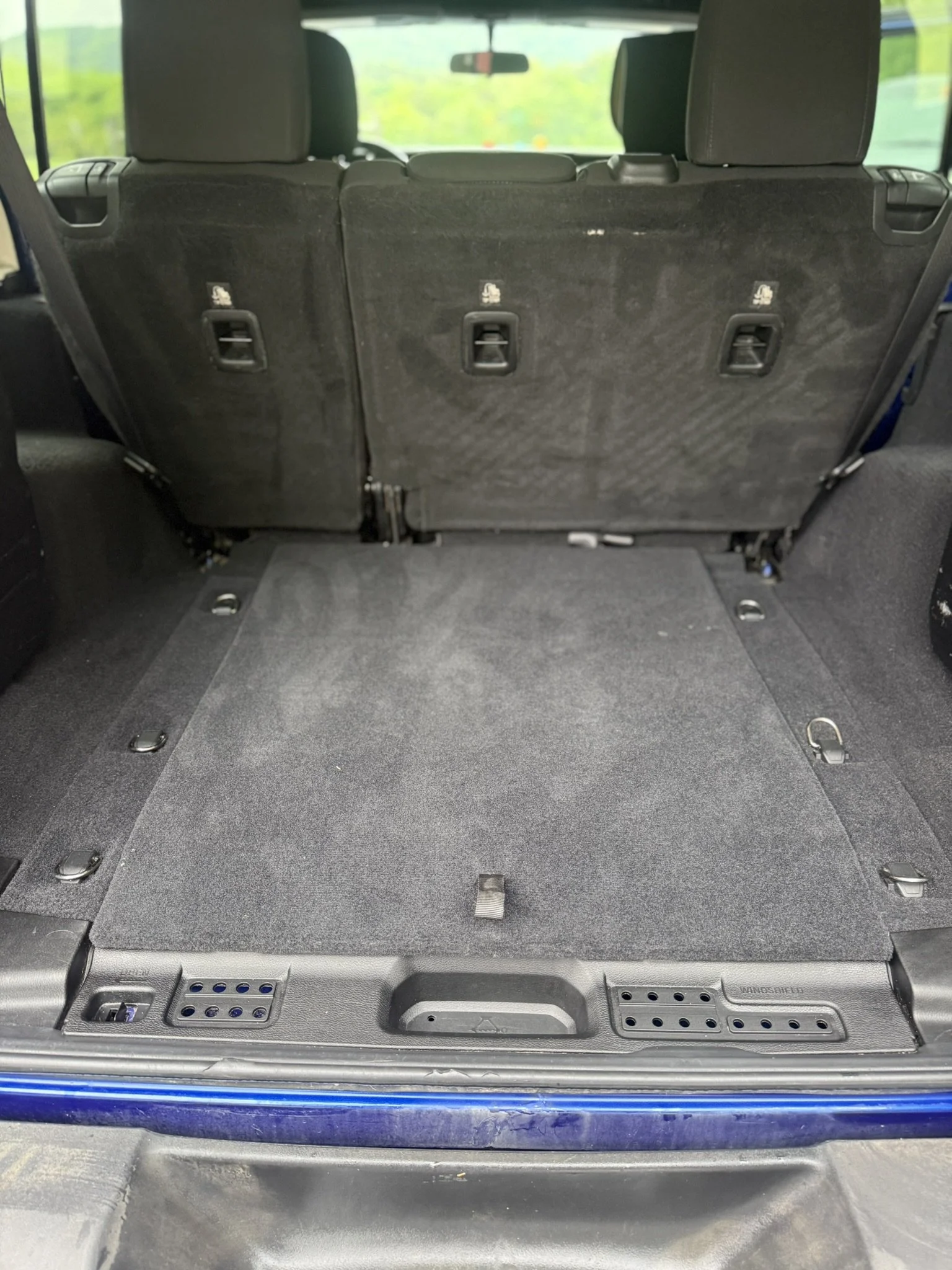 The image shows the interior of a vehicle with the rear seats folded down, revealing a flat cargo area with tie-down hooks and a textured surface.