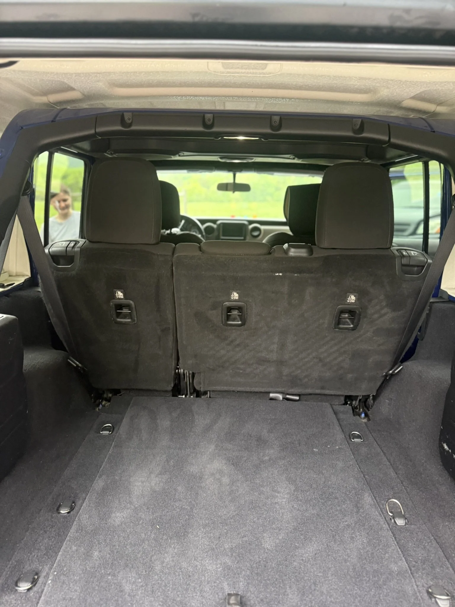 The rear interior of a vehicle showing the cargo space with folded seats and a flat black carpeted floor.