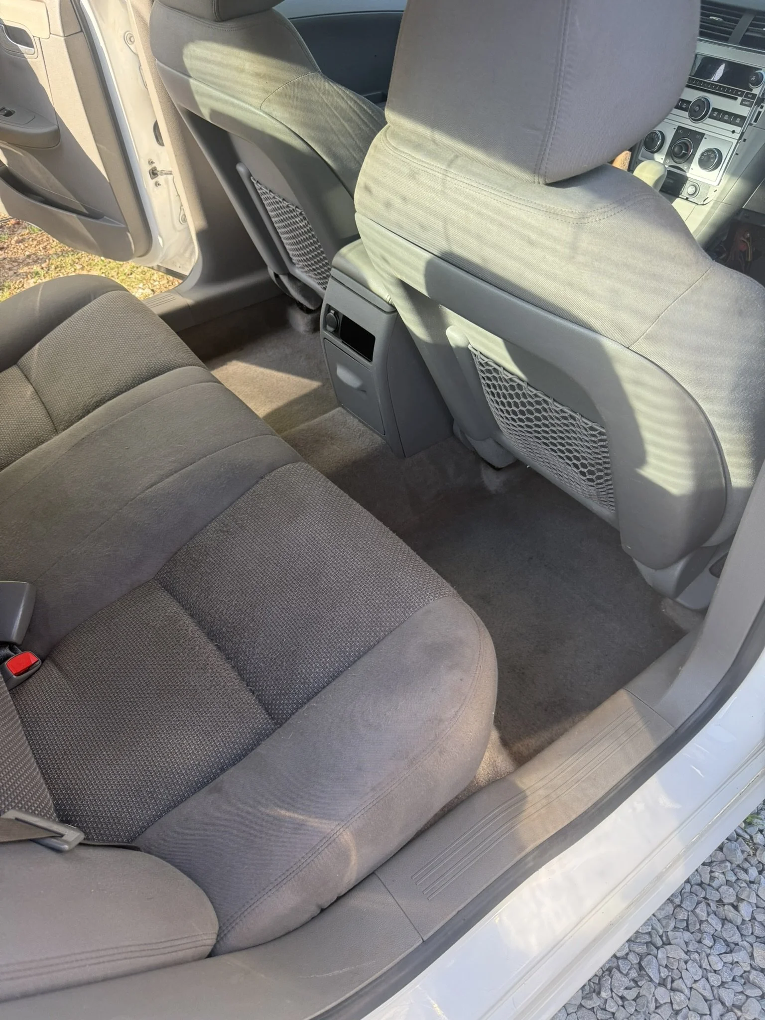 View of the interior of a car showing the back seat with gray fabric upholstery, the front seatbacks, and part of the dashboard.