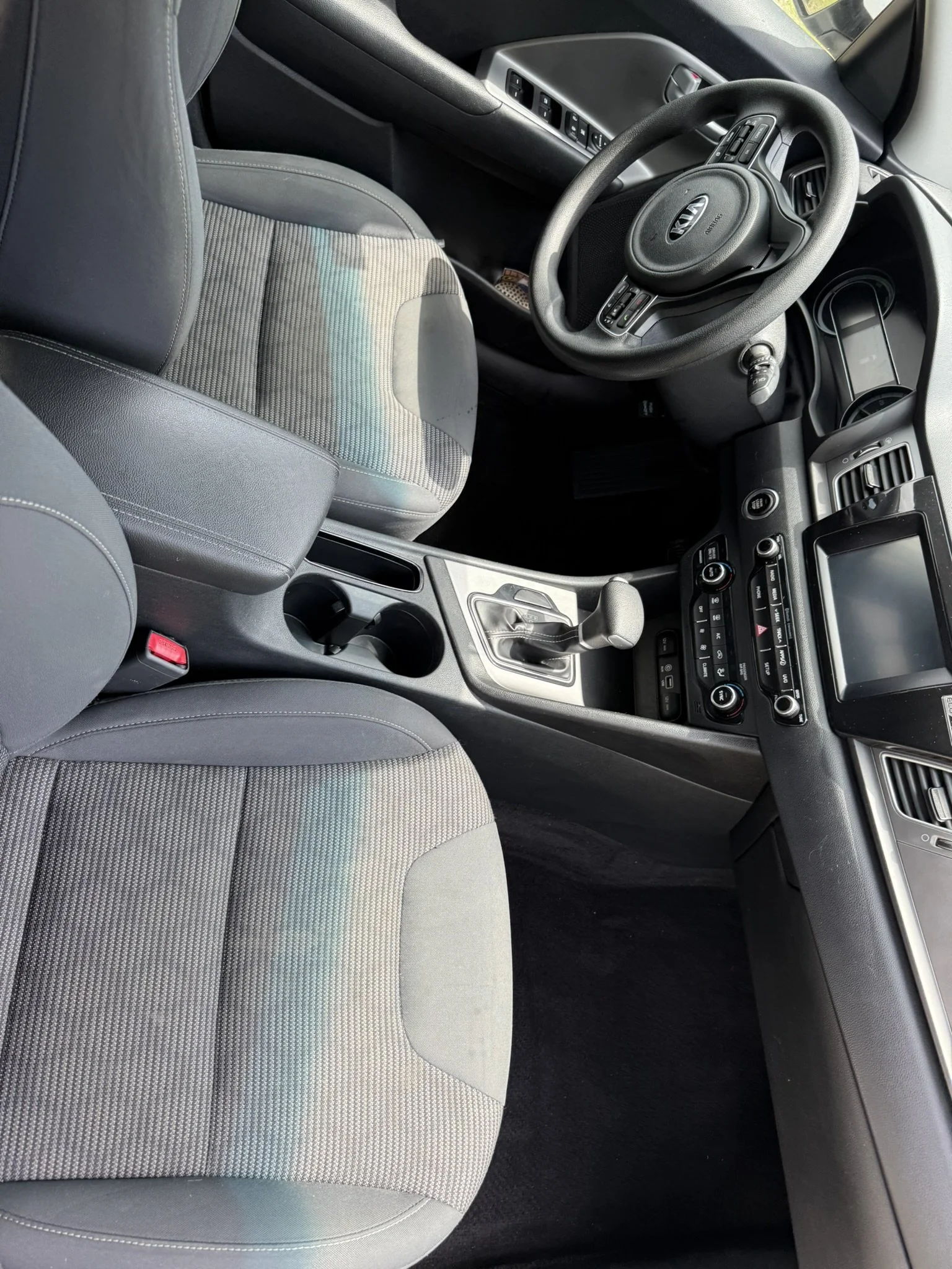 Interior view of a car showing the driver's seat with gray upholstery and the steering wheel with the Kia logo.