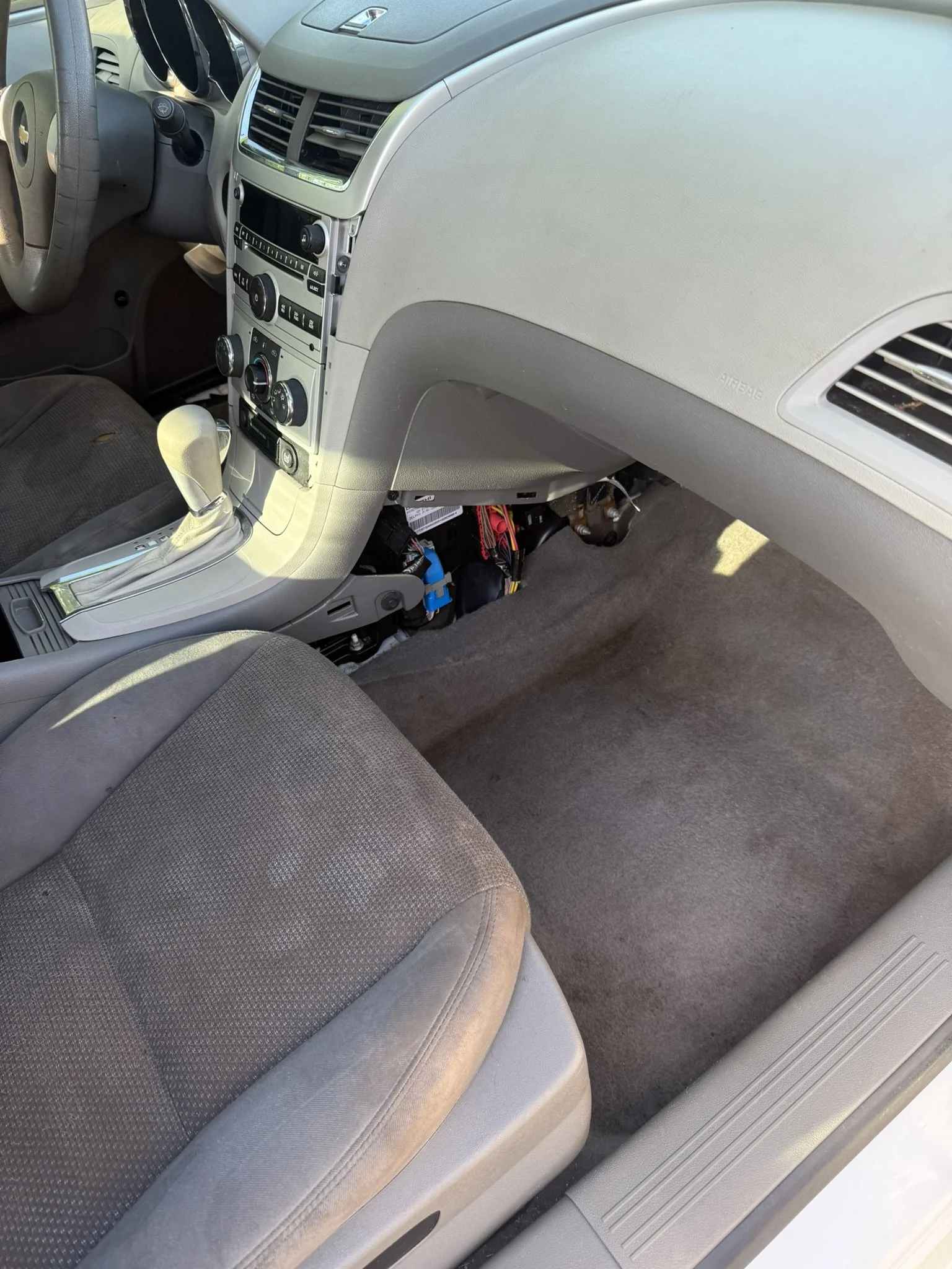 The photo shows the interior of a car, including the gray seat, the dashboard, and the gear shift.