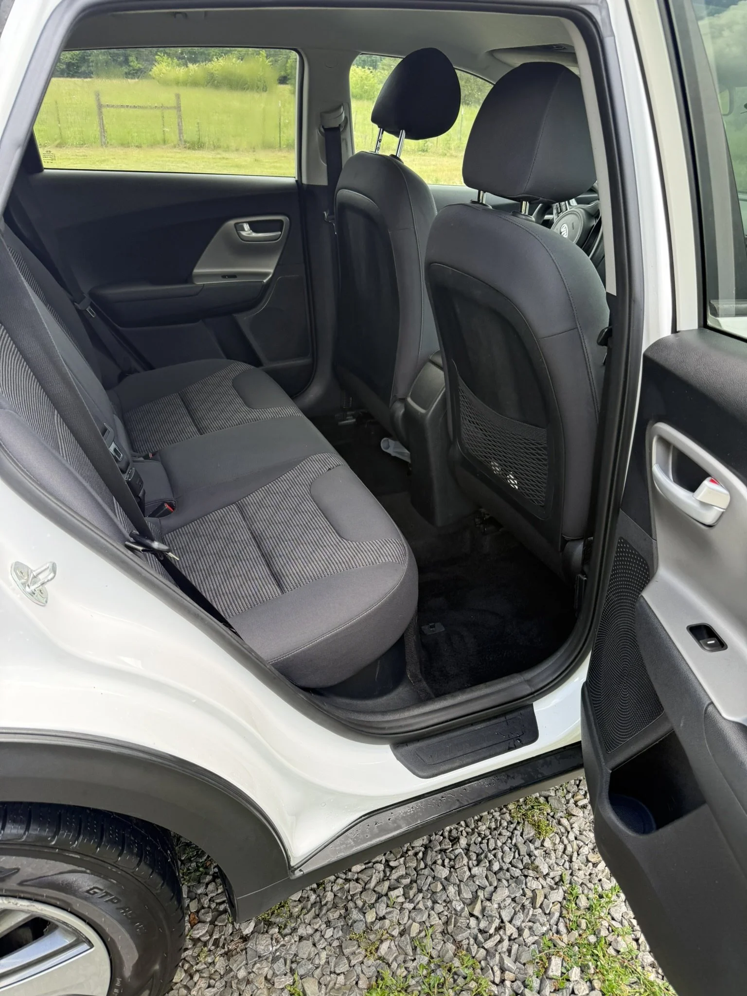 The interior of a white vehicle showing the front and rear passenger seats, with a view of a green outdoor area through the windows.